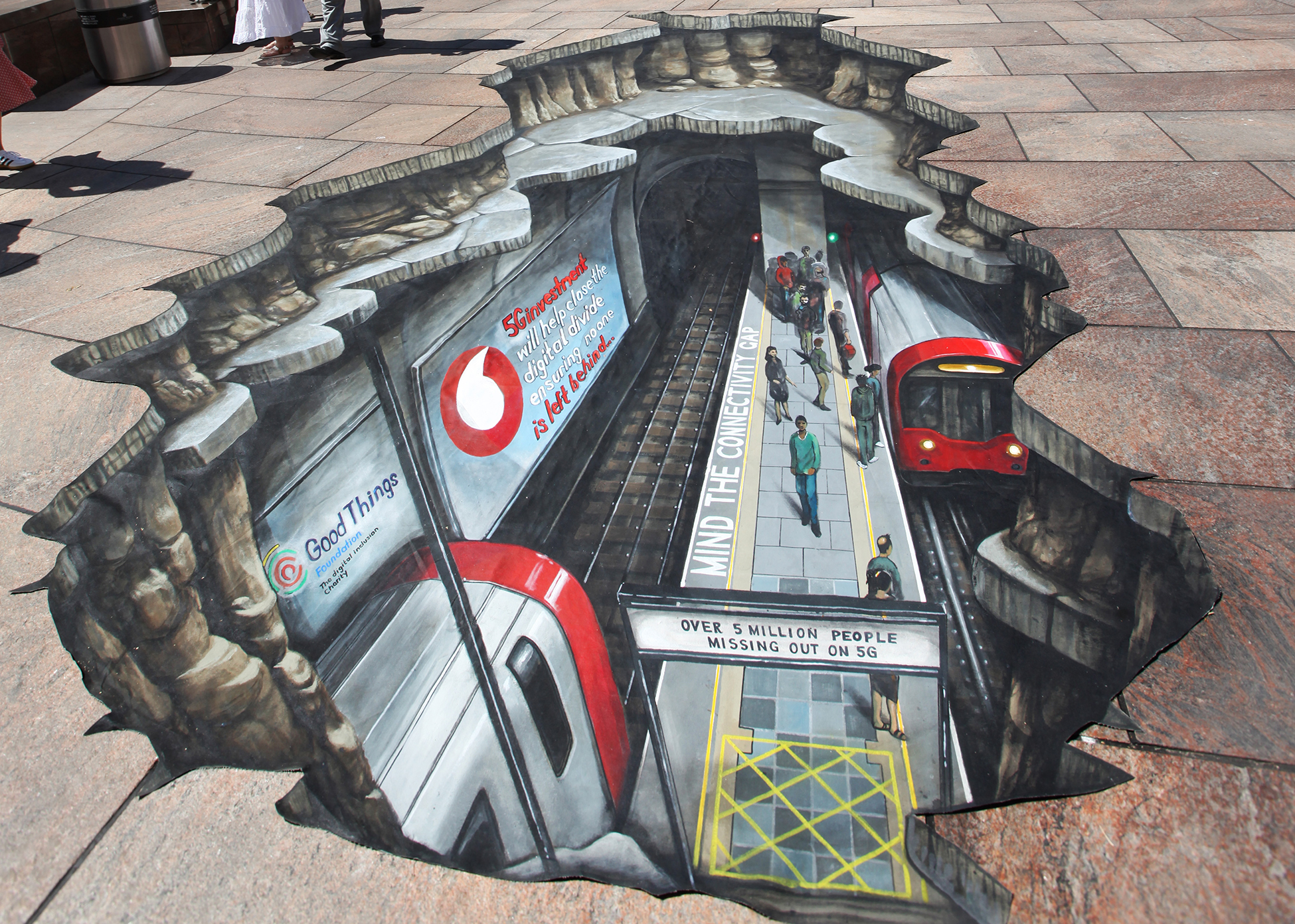 Painting on the ground in London centre of the underground, with billboards of Good Things and Vodafone logos, stating '5G will help close the digital divide, ensuring no one is left behind...' with a sign on the platform reading 'over 5 million people missing out on 5G'.