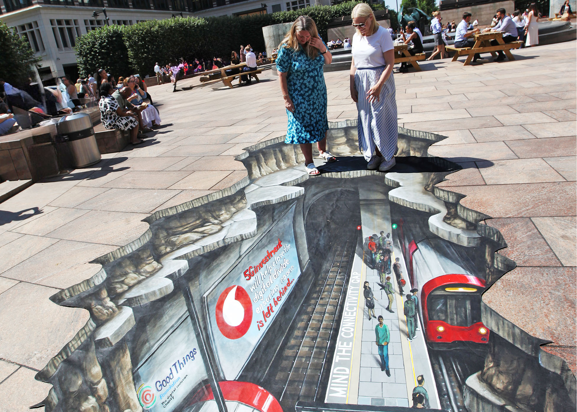 Good Things' CEO Helen Milner stands over a ground mural that illustrates a gap into the tube station below London. Text is painted on the mural that says mind the 5G connectivity gap.