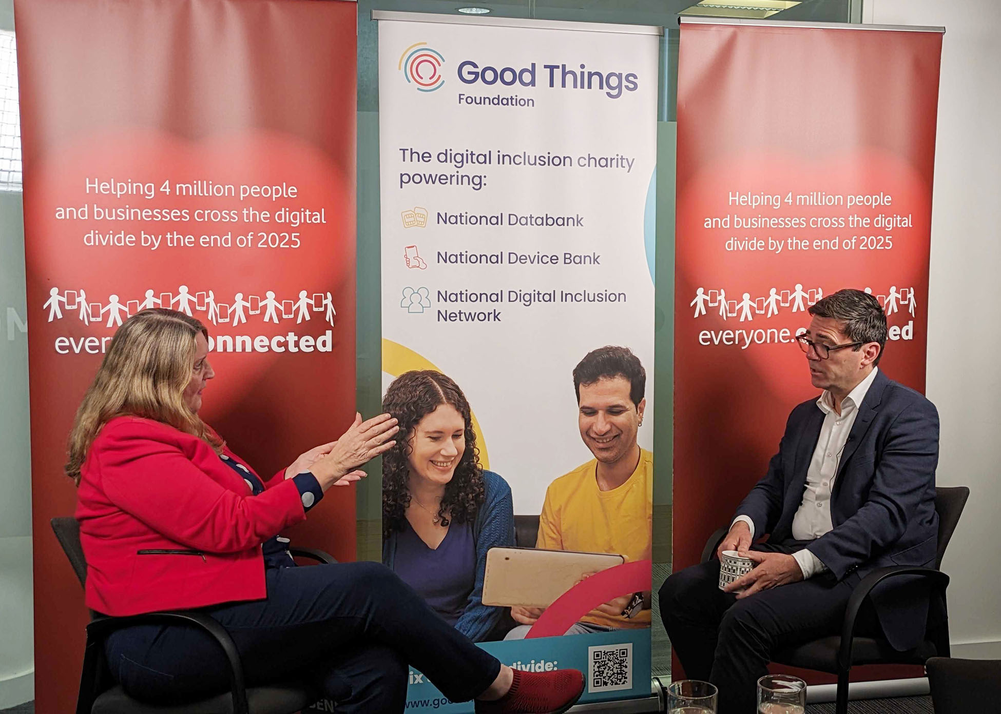 Helen Milner OBE, CEO of Good Things, is in a fireside chat conversation with Greater Manchester Mayor Andy Burnham. They're sat in front of a large banner that says Good Things Foundation, the digital inclusion charity powering the National Databank, National Device Bank and National Digital Inclusion Network.
