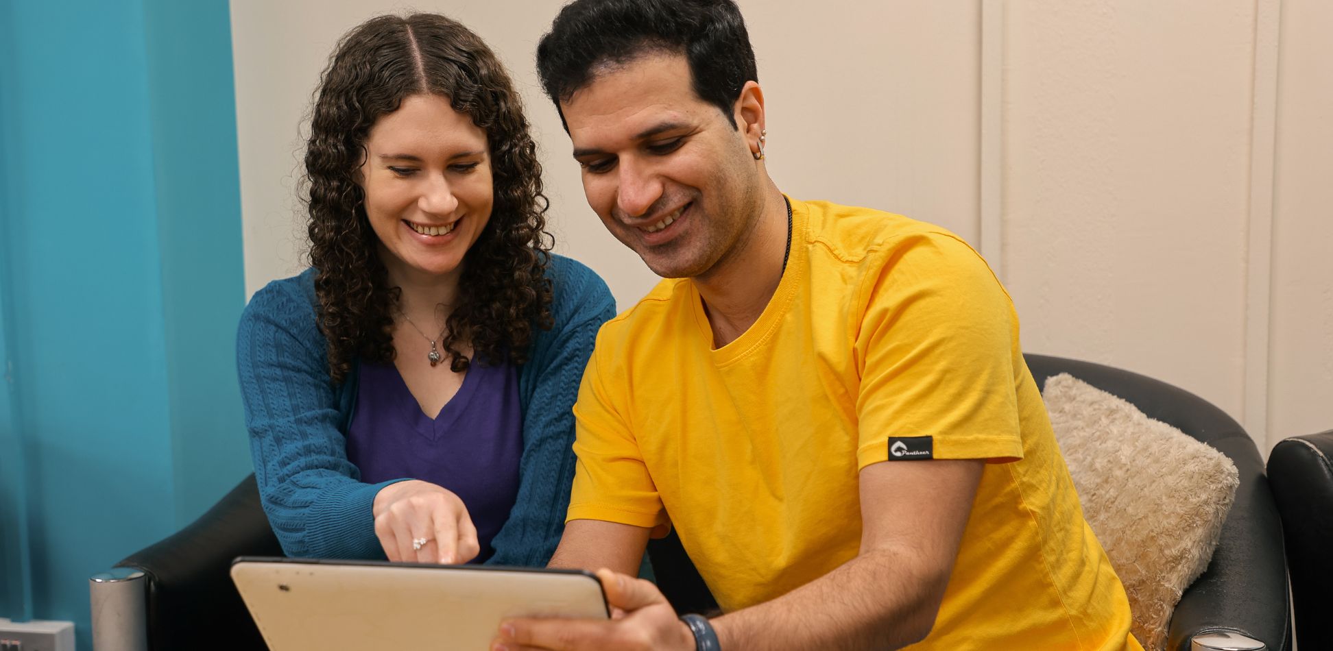 Hayley, in teal, teaching Sam, in yellow, how to use a tablet.