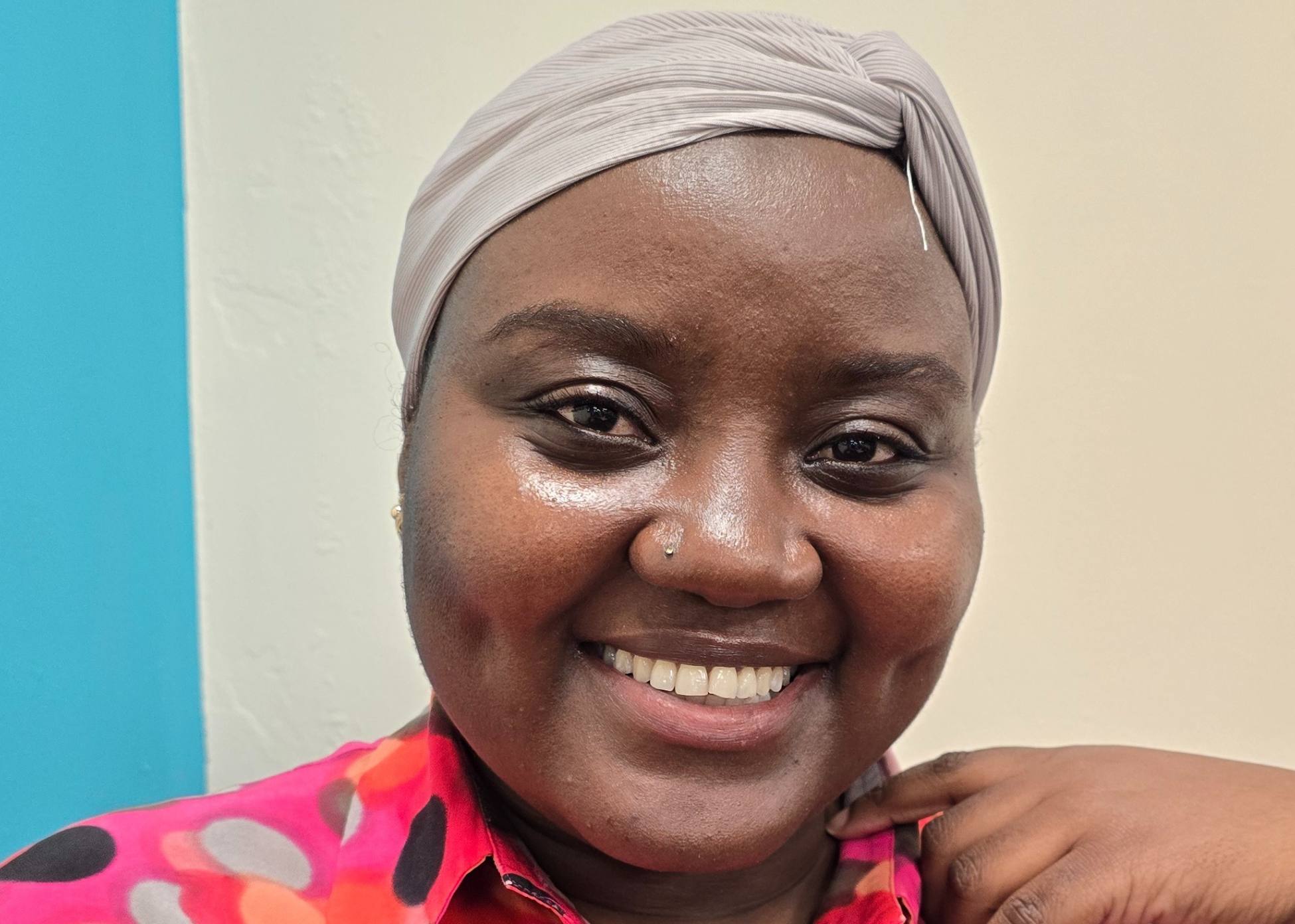 A person looking towards the camera and smiling, wearing a bright pink patterned blouse.