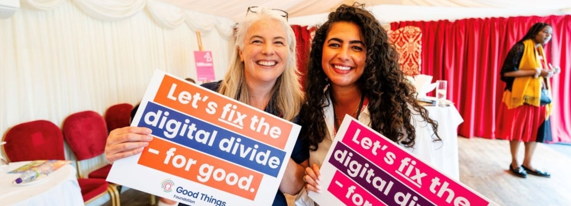 Two women holding signs that say Let's Fix The Digital Divide - For Good.